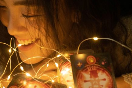 Woman smiling beside tarot cards illuminated by warm lights