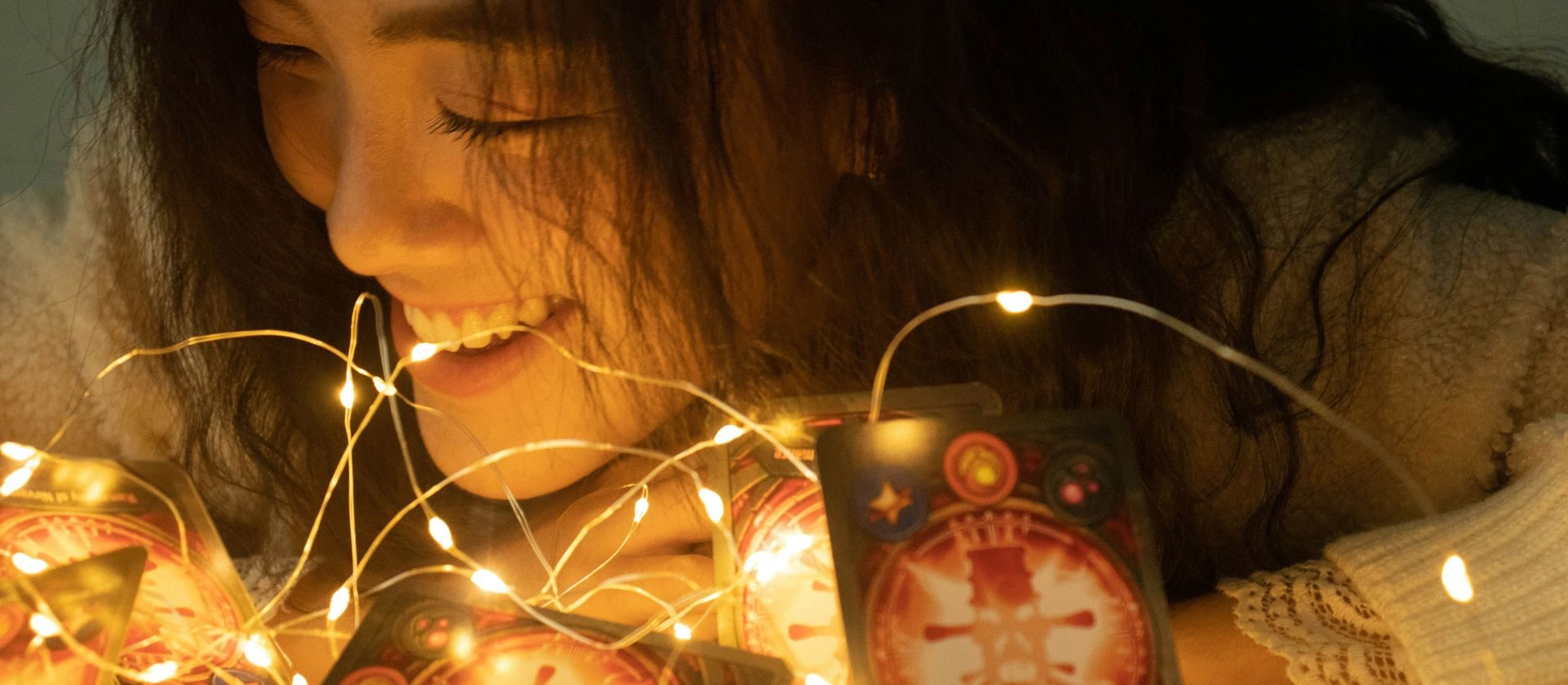Woman smiling beside tarot cards illuminated by warm lights